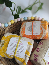 Load image into Gallery viewer, Flour sack cotton tea towels with brightly colored flower and citrus prints shown in a basket. There is one with oranges, one with black eyed susan flower, lavender, and poppy prints.