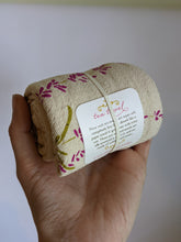 Load image into Gallery viewer, Green and purple lavender flower print on unbleached cotton tea towel. Tea towel is held in hand, rolled up with tag showing 100% cotton, lint free, made in USA.