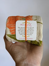 Load image into Gallery viewer, Orange and green print of poppy flowers on unbleached cotton makes this cute tea towel for your kitchen. The tag shown here tells you it is made in USA and screenprinted. They get better with each use. Lint free.