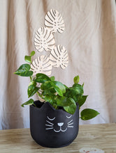 Load image into Gallery viewer, black, six inch planter pot that looks like a cat is shown holding a golden pothos plant that is climbing up the monstera leaf shaped trellis.  Trellis is the featured item for sale.