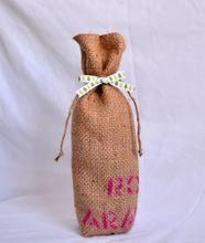 Cargar imagen en el visor de la galería, Burlap wine bag with pink text on the bottom half. This is made from recycled coffee bean sack. The text originally told the origin of the coffee . It ties shut with a festive ribbon.