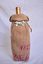 Cargar imagen en el visor de la galería, Burlap wine bag with pink text on the bottom half. This is made from recycled coffee bean sack. The text originally told the origin of the coffee . It ties shut with a festive ribbon.