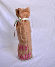 Cargar imagen en el visor de la galería, Burlap wine bag with pink text on the bottom half. This is made from recycled coffee bean sack. The text originally told the origin of the coffee . It ties shut with a festive ribbon.