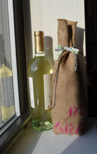 Cargar imagen en el visor de la galería, Burlap wine bag next to wine bottle to show scale of size. Bag is made from recycled coffee bean sack with pink text visible at the bottom half of it. Pink text originally told origin of coffee.