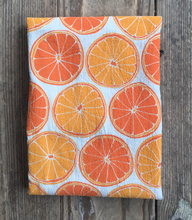 Load image into Gallery viewer, Light and dark orange colors make up the pattern of sliced oranges on an unbleached cotton tea towel 
