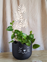 Load image into Gallery viewer, black, six inch planter pot that looks like a cat is shown holding a golden pothos plant that is climbing up the monstera leaf shaped trellis.  Trellis is the featured item for sale. 

