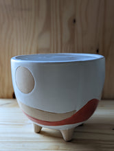 Cargar imagen en el visor de la galería, Boho/Southwest style desertscape planter , 6 inch ceramic footed pot. White glaze over tan features a sun with hand painted wavy lines in tan and red orange to represent the desert scape. 
