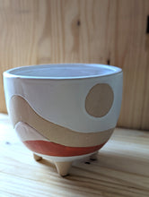 Cargar imagen en el visor de la galería, Plant pot, Boho/Southwest style desertscape planter , 6 inch ceramic footed pot. White glaze over tan features a sun with hand painted wavy lines in tan, light pink, and  red orange to represent the desert scape. 
