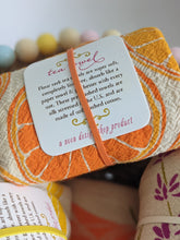 Load image into Gallery viewer, Flour sack tea towel with citrus oranges print shown rolled up with a cute tag on it showing they&#39;re lint free, 100% cotton, made in USA. 
