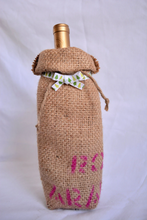 Cargar imagen en el visor de la galería, Burlap wine bag with pink text on the bottom half.  This is made from recycled coffee bean sack. The text originally told the origin of the coffee . It ties shut with a festive ribbon.
