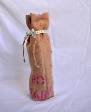 Cargar imagen en el visor de la galería, Burlap wine bag with pink text on the bottom half.  This is made from recycled coffee bean sack. The text originally told the origin of the coffee . It ties shut with a festive ribbon.
